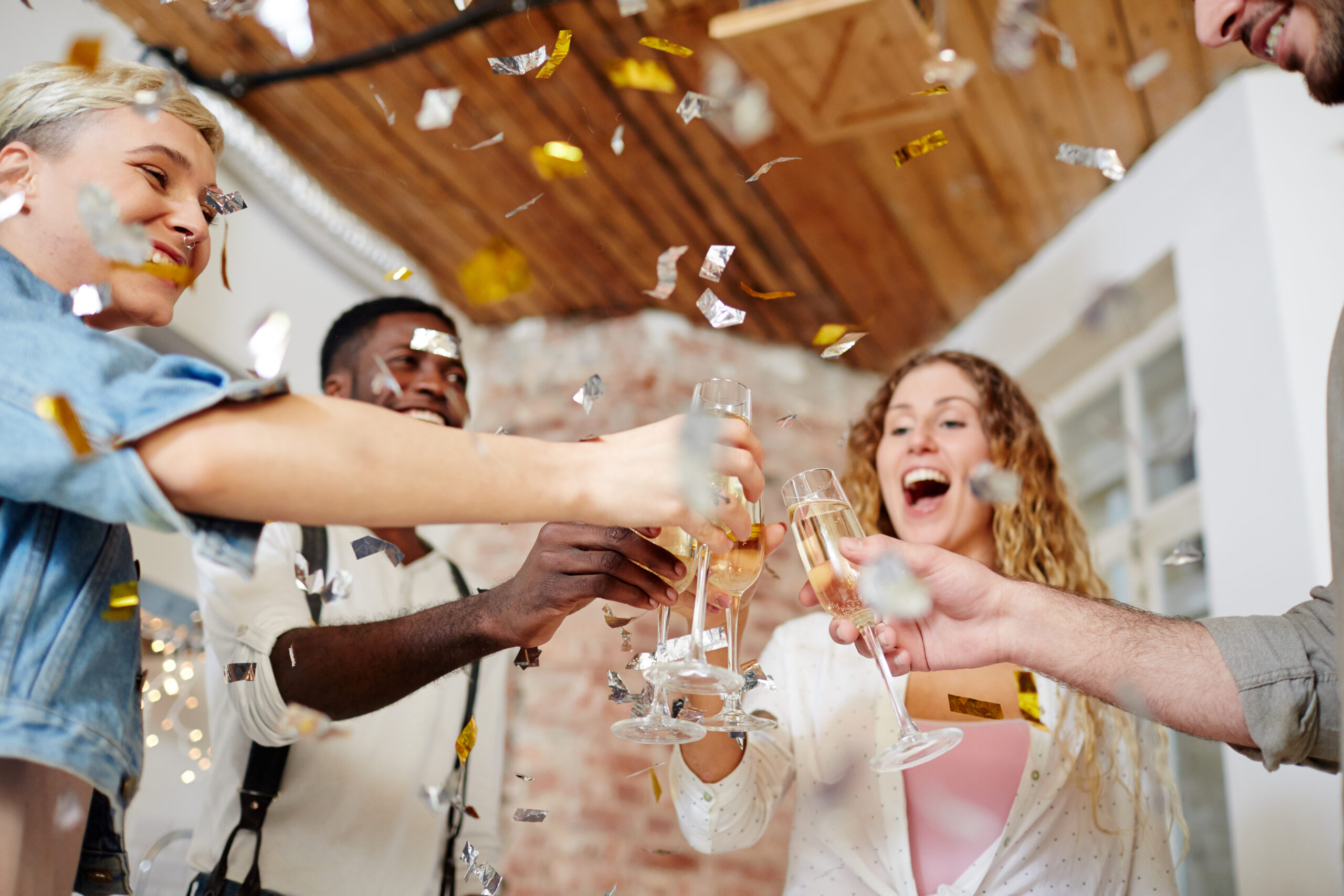 Group of excited friends cheering up with flutes of champagne at party